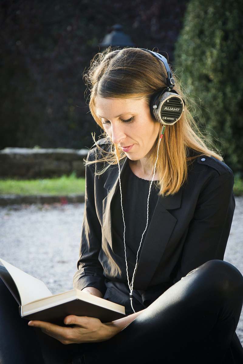 human selective focus photography of sitting woman wearing headphones while reading book sitting