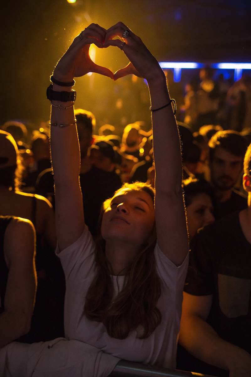 human woman at crowd raising her hand while making heart sign people