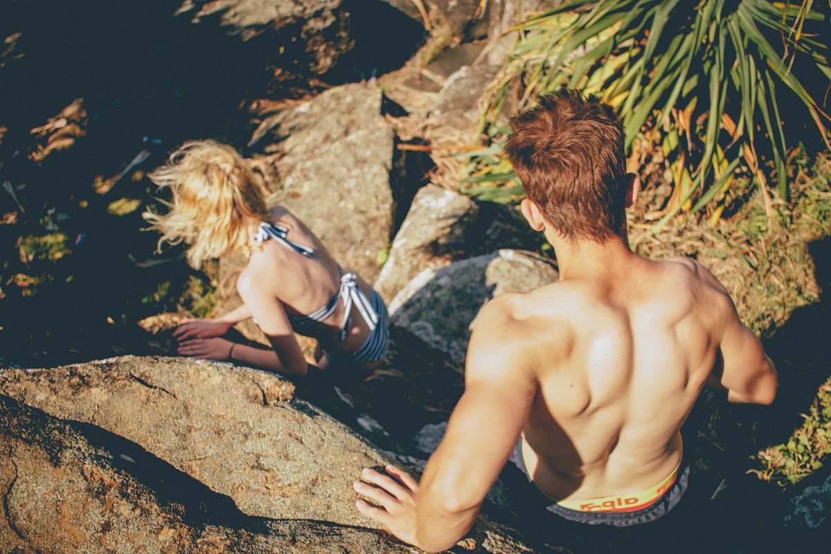 person Couple in swimwear climbing down the rocky cliff at Kings Beach woman