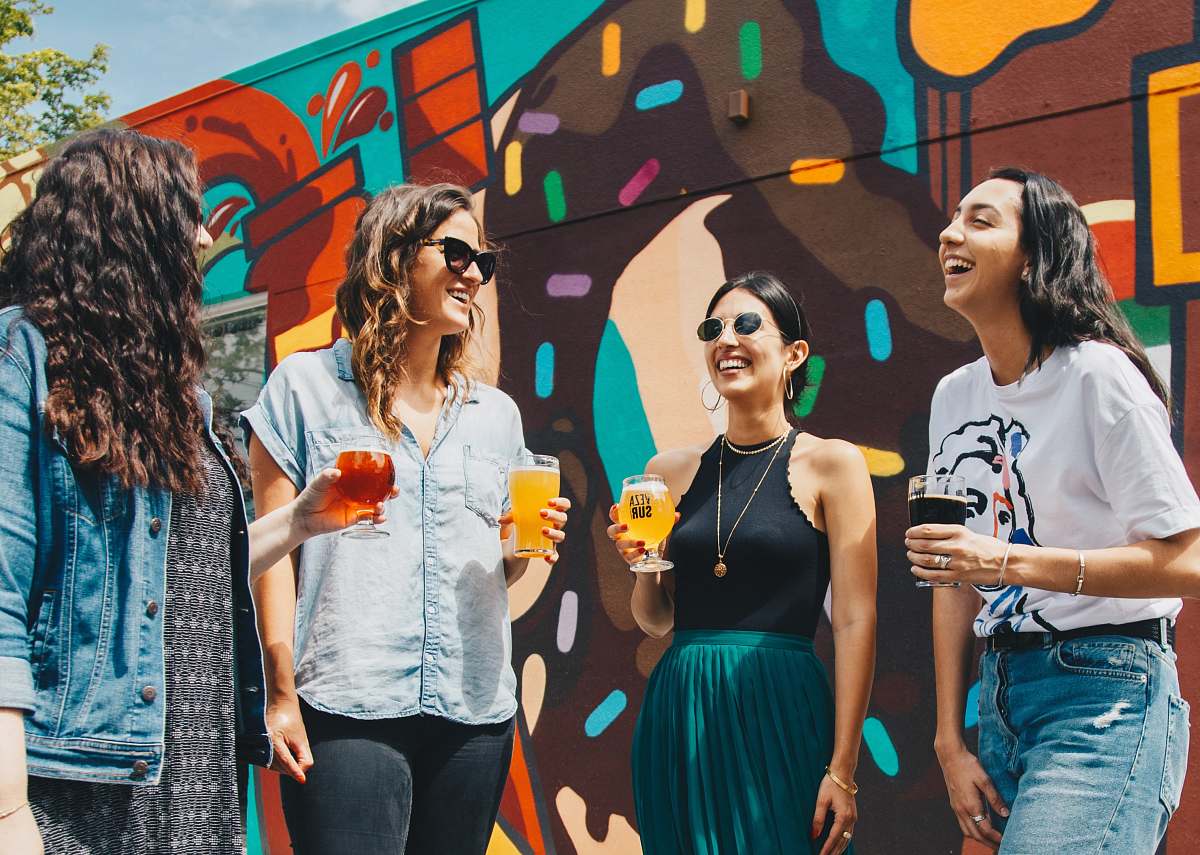 person four women holding drinks while laughing together during daytime human
