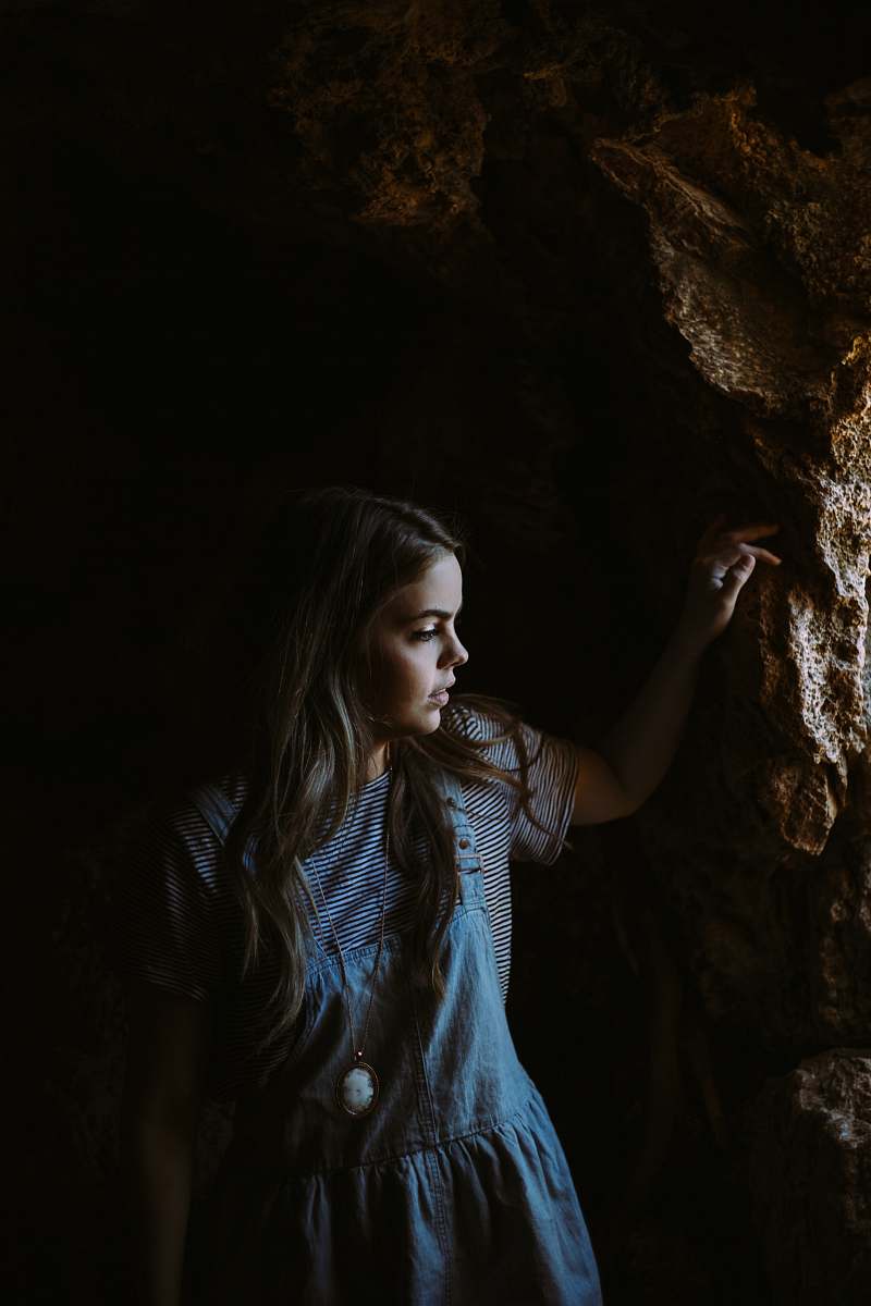 girl girl wearing blue and white dress holding on brown rocks cave