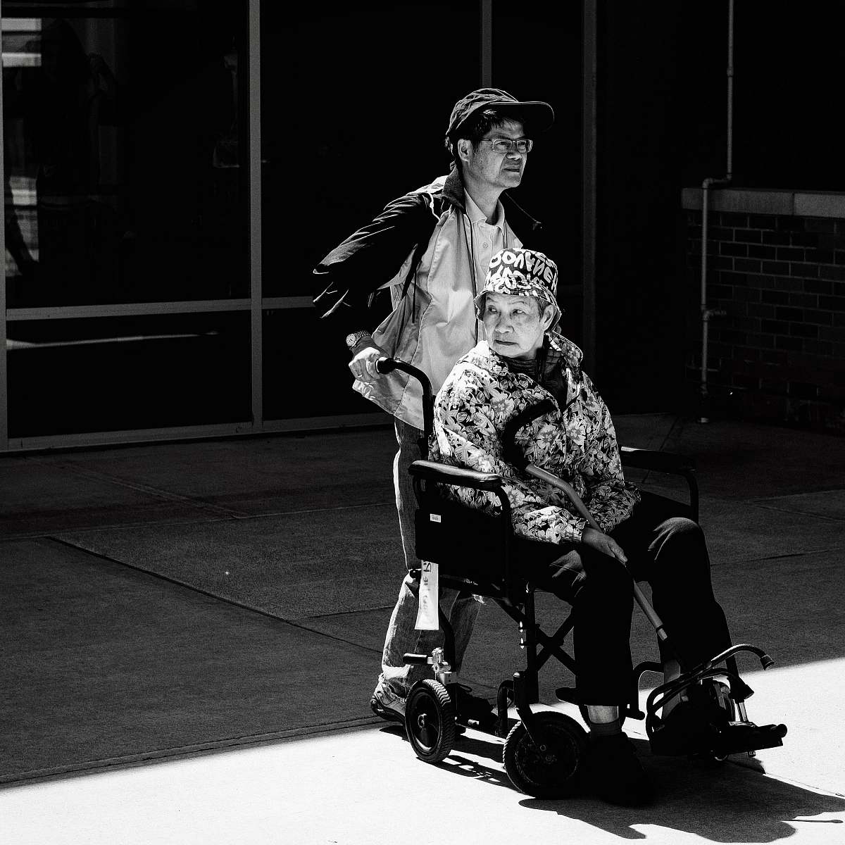 black-and-white gray scale photo of man pushing wheelchair wheelchair