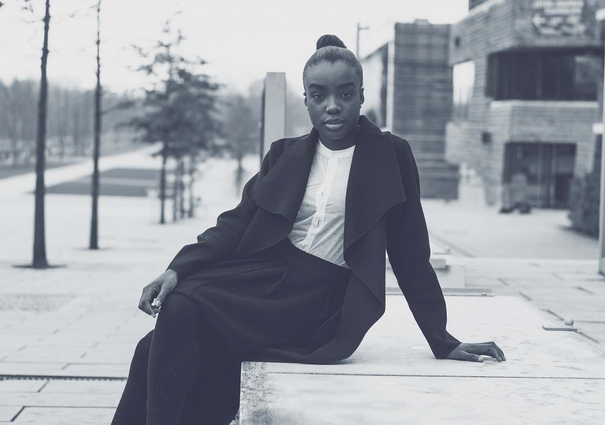 woman grayscale photo of woman sitting on concrete pavement near building grey