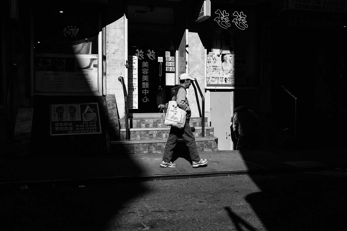 person grayscale photography of person walking beside building black-and-white