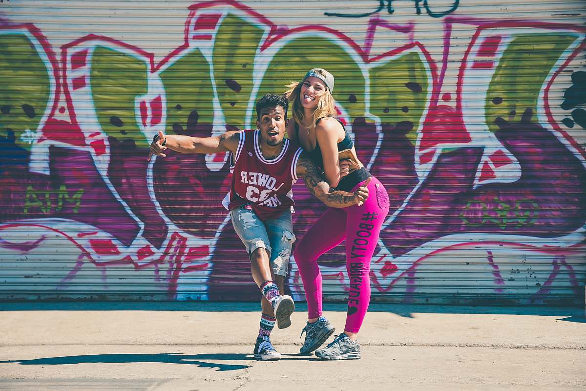 This vibrant scene captures a graffiti artist joyfully posing beside two young women engaged in an energetic game of basketball. The striking mural in the background adds an urban flair, making this image perfect for promoting sports, youth culture, and street art. Ideal for blogs, advertisements, and social media campaigns aimed at showcasing the lively spirit of city life.