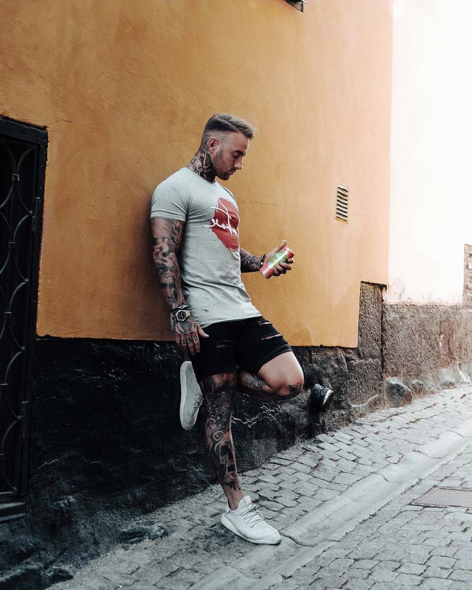 person man covered with tattoo leaning on wall holding can during daytime human