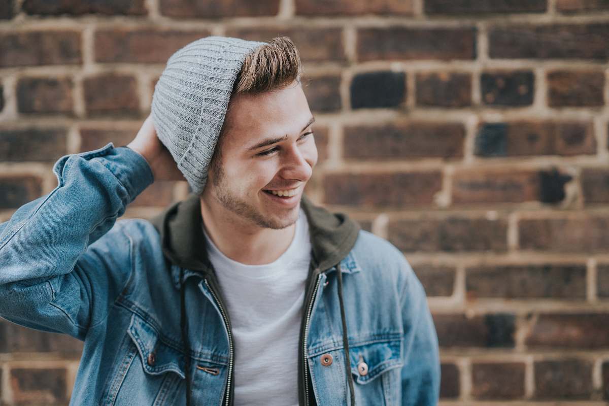 person man holding the back of his head while smiling near brick wall human