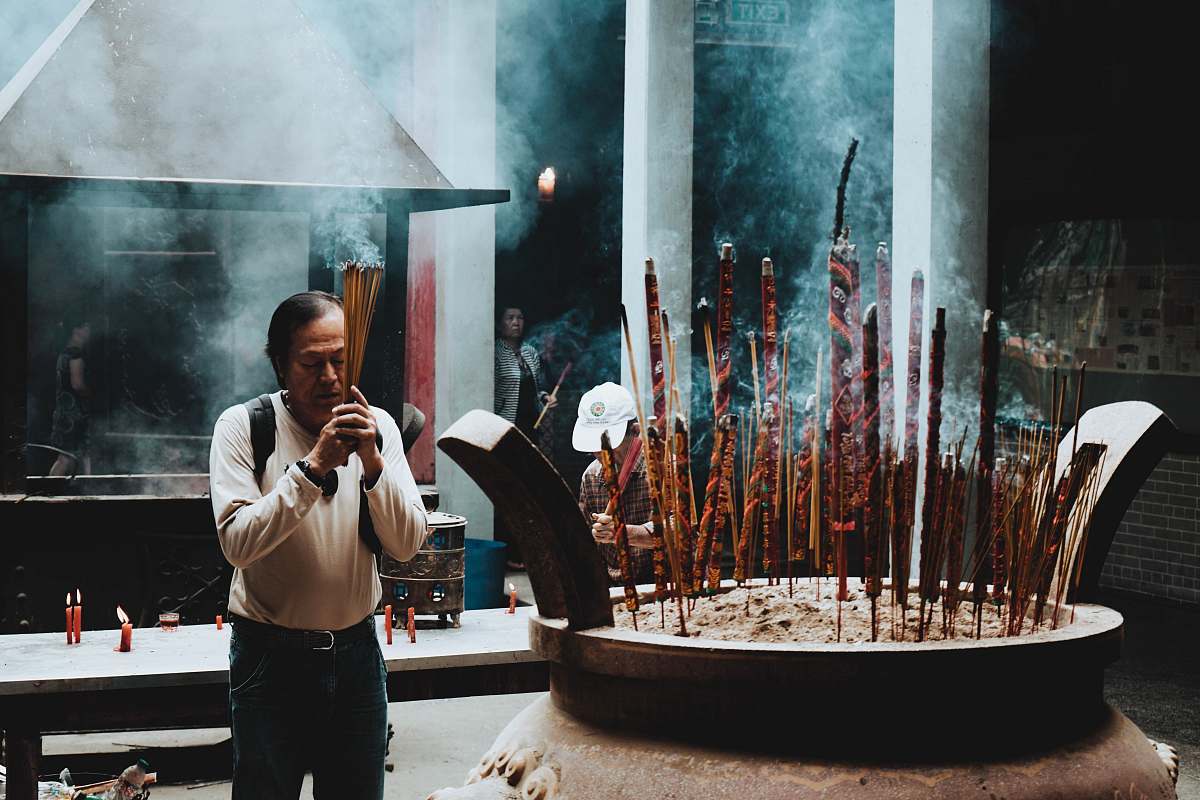 person man in beige long-sleeved shirt in praying gesture incense