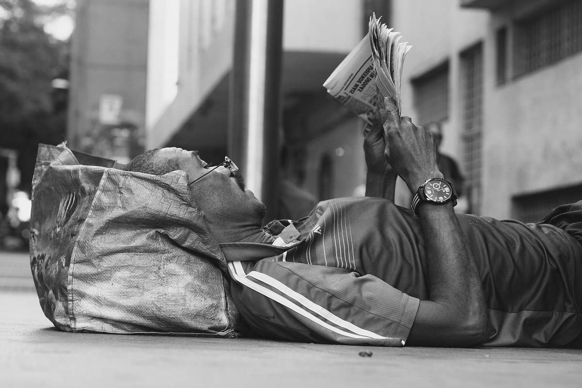 person man lying on sidewalk reading newspaper black-and-white