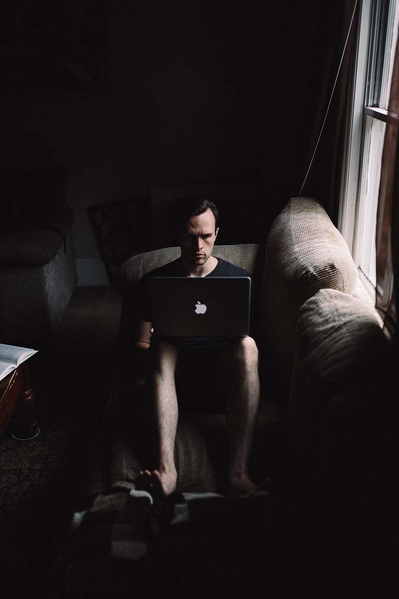 human man seating on sofa using MacBook beside window person
