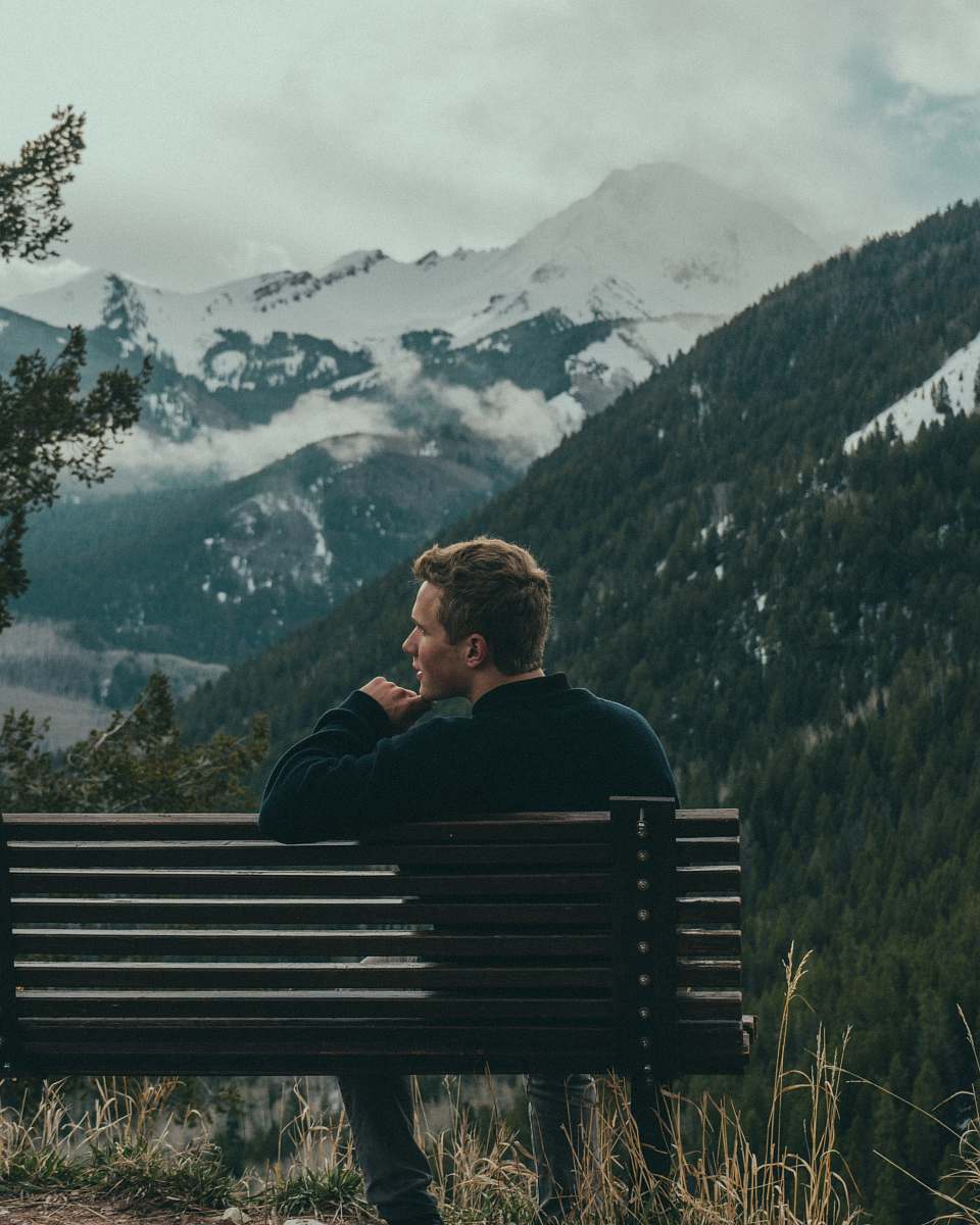 person man sitting on bench on top of the mountain trees