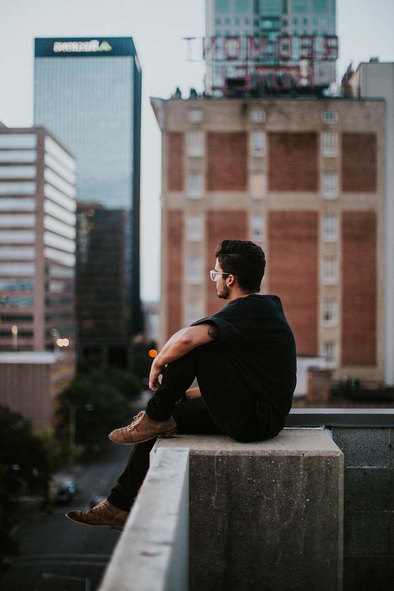 person man sitting on white concrete building during daytime human