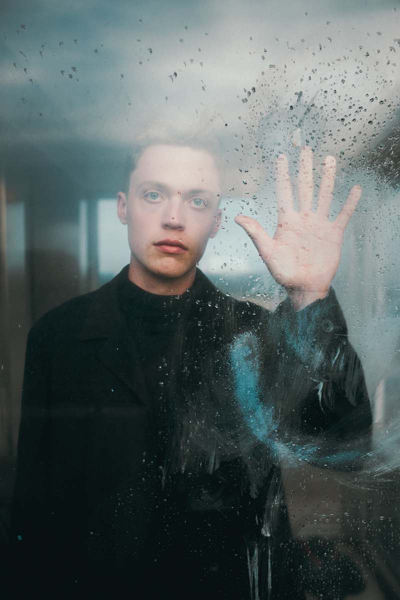 person man standing in front of glass wall while touching it during daytime human