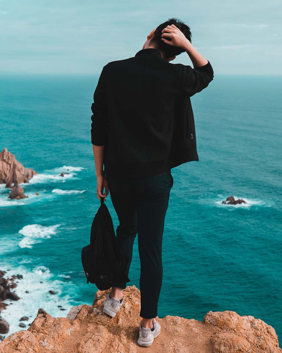 person man standing on top of mountain facing backwards at body of water human