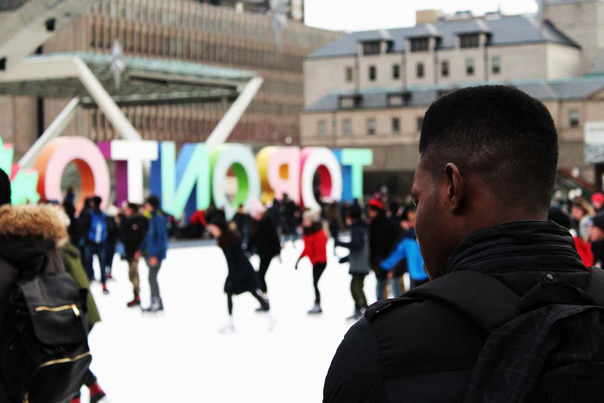 toronto man wearing black backpack ice skating with other people near Toronto freestanding decor during daytime crowd