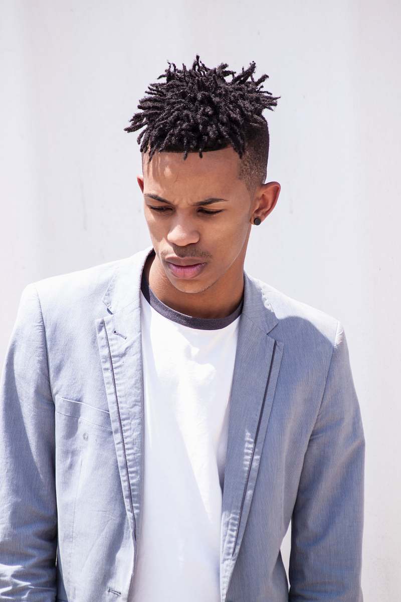person man wearing blue notched lapel suit jacket and white crew-neck shirt standing behind white painted surface at daytime human