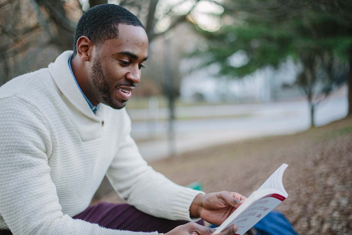 reading man wearing white sweater while reading book read