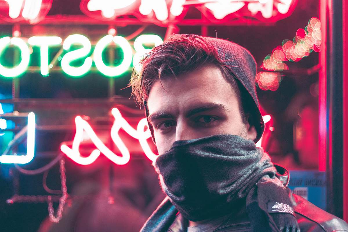 person man with face half covered with mask standing in front of red and green neon light signage during daytime human