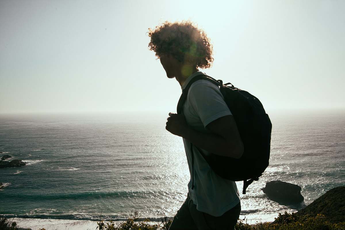 person men wearing white-crew-neck t-shirt and black backpack watching the ocean human