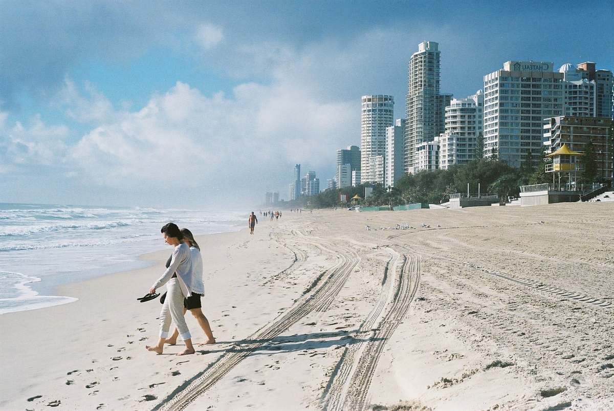 beach people walking on seashore near concrete buildings during daytime sand
