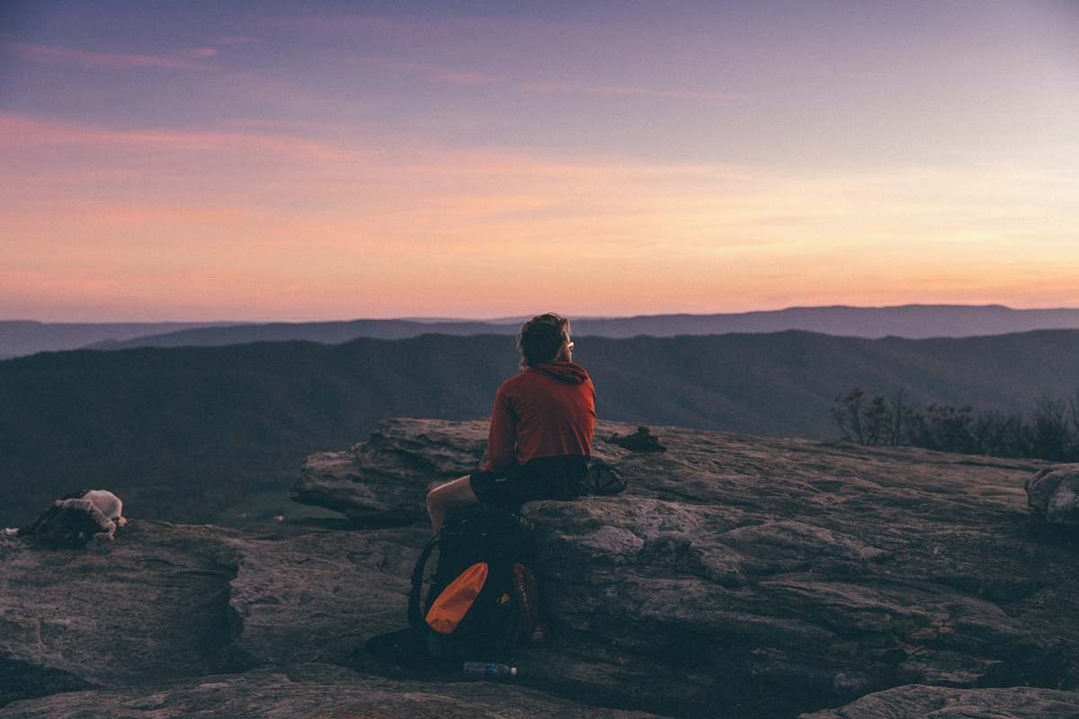 person person sitting on boulder overlooking mountain during golden hour human