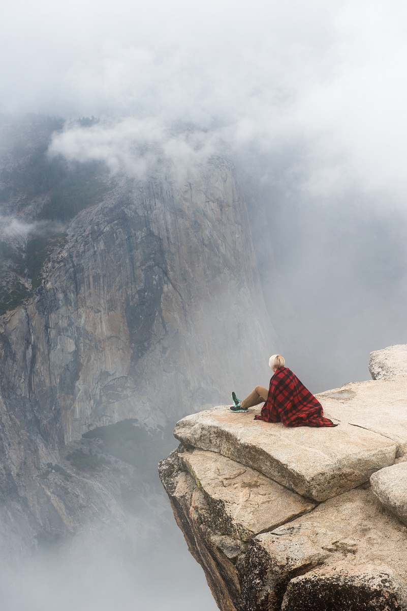 person person sitting on cliff under cumulus cloud human