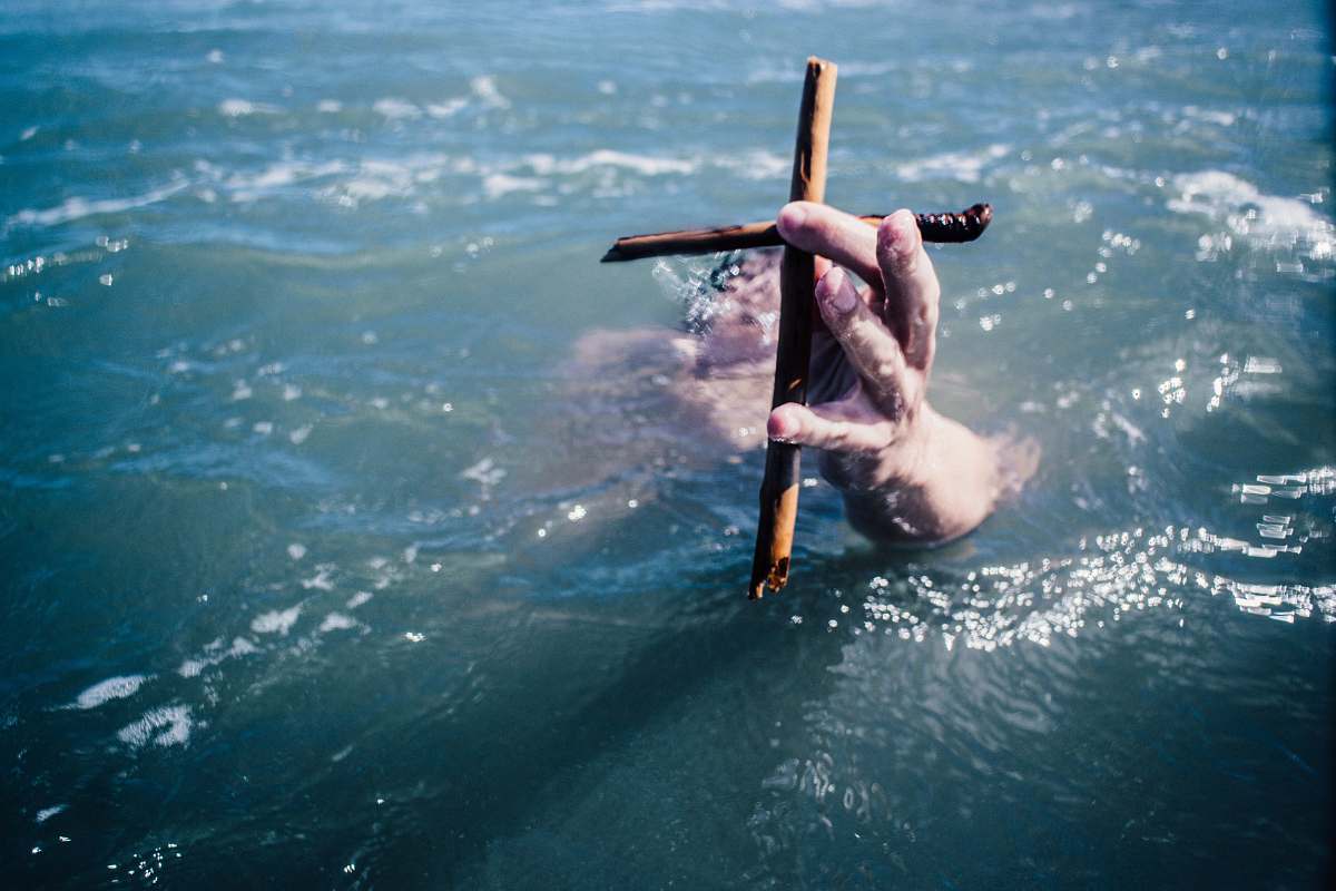 person person under water holding brown wooden cross above water at daytime cross