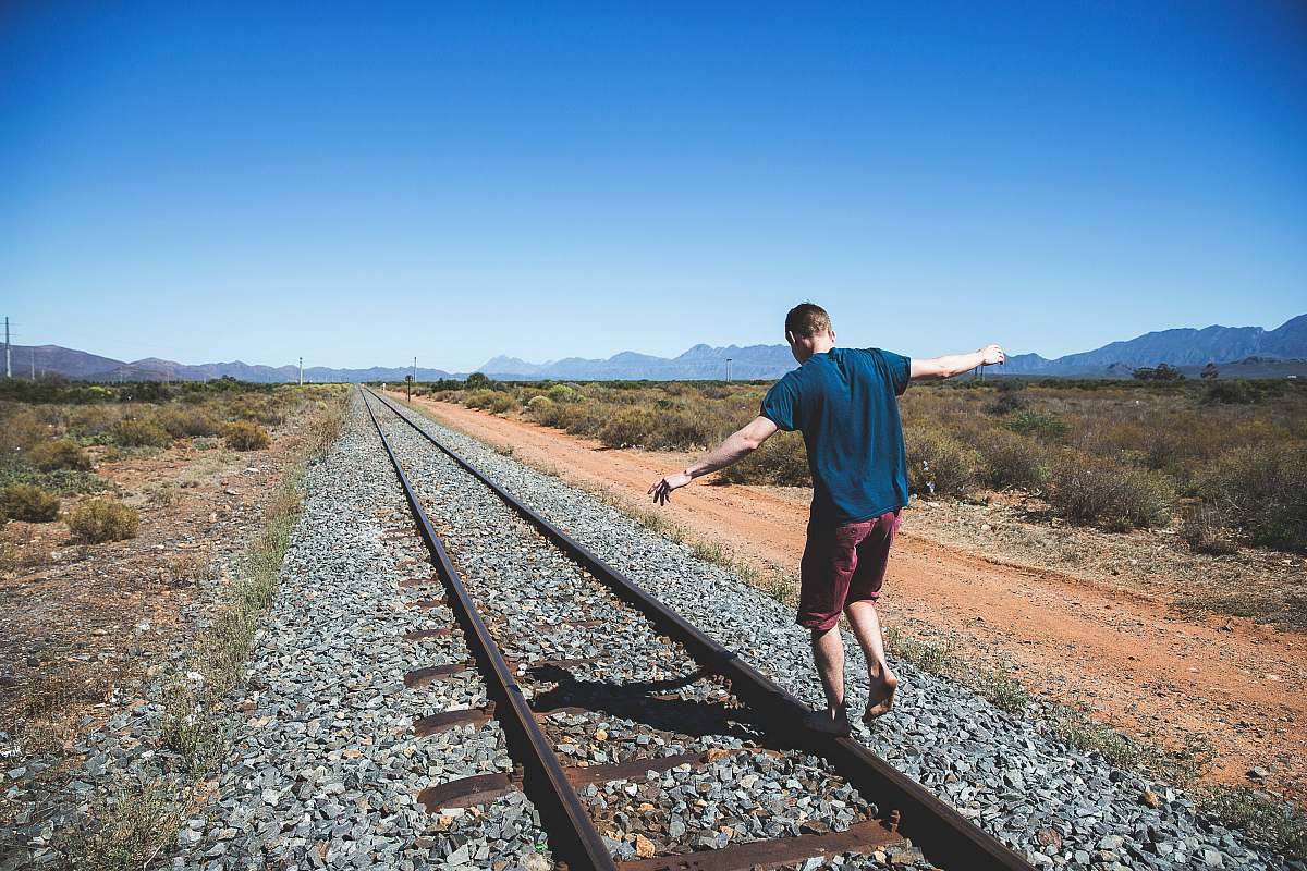 person person walking on brown steel train rail outdoor during daytime railway