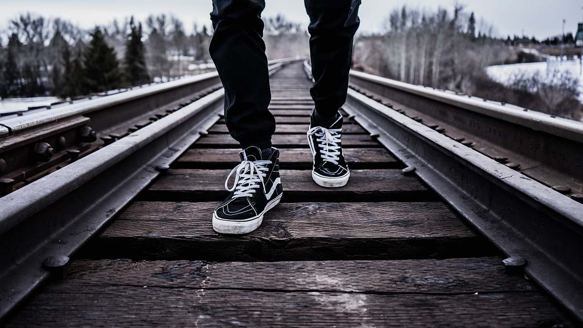 person person wearing pair of black-and-white Vans Old Skool shoes walking on brown train tracks during winter human
