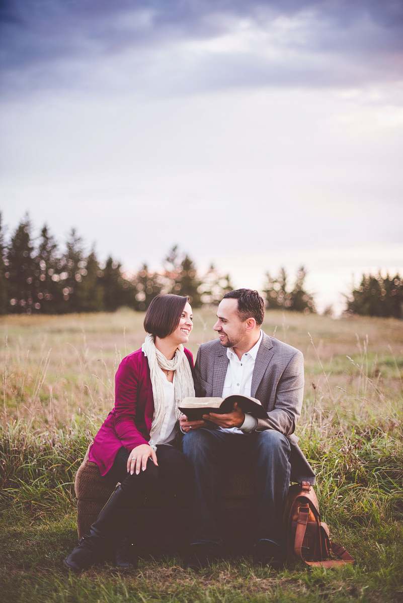 person photo of man reading book to woman under grey cloudy sky couple