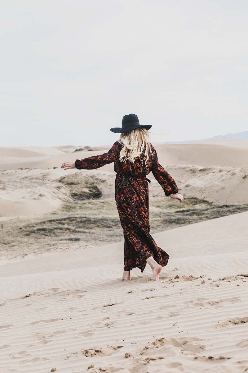 person photo of person wearing brown and orange floral maxi dress walking barefooted along deserted land woman