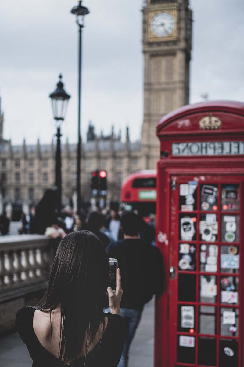 london selective focus of woman taking pictures in front of red payphone bus