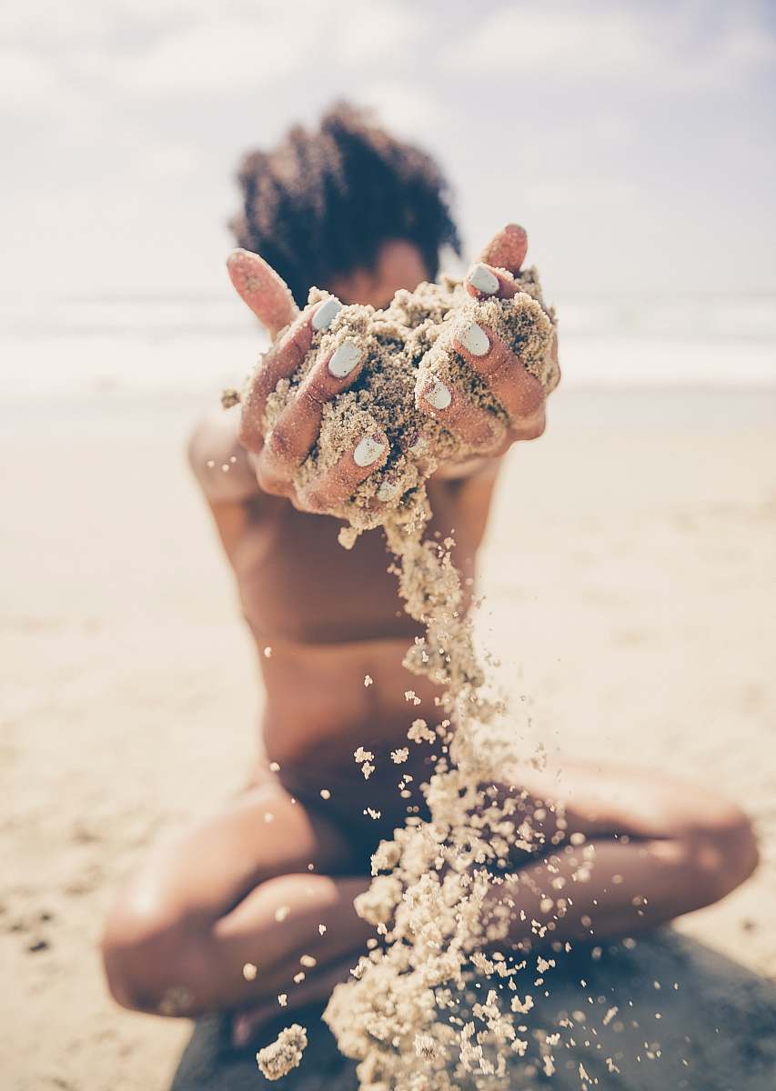person selective focus photo of woman sitting and raising sand during daytime beach