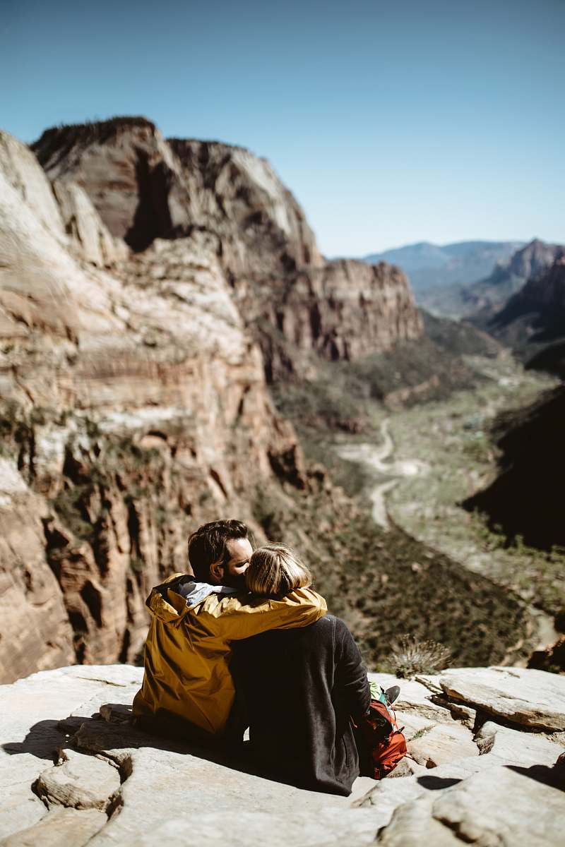 couple selective focus photography of couple sitting on rock fall under sunlight love