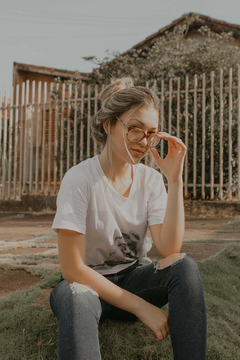 person shallow focus photography of woman sitting on grass while holding her eyeglasses human