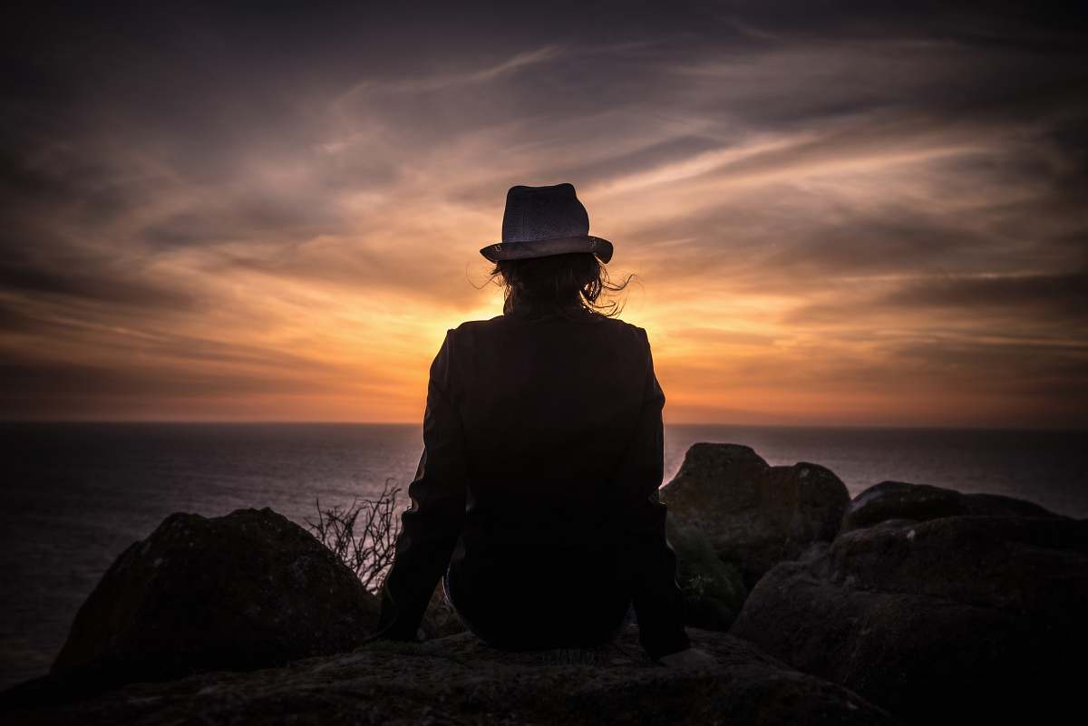 person silhouette of man sitting on stone looking at body of water human