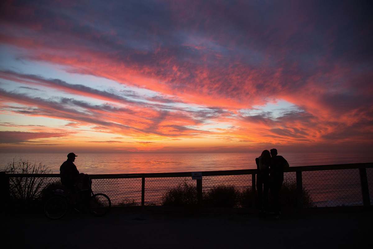 silhouette silhouette of people near cliff railings at distance to wide body of water during golden hour sunrise