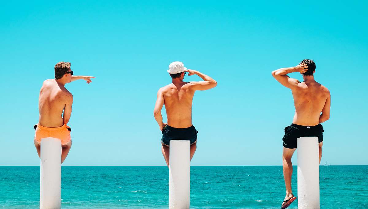 person three men's sitting on white concrete bollard near body of water during daytime human