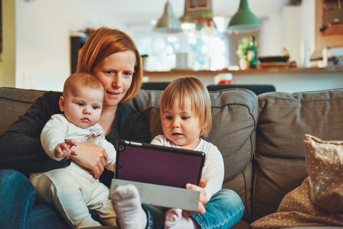 kid two babies and woman sitting on sofa while holding baby and watching on tablet family