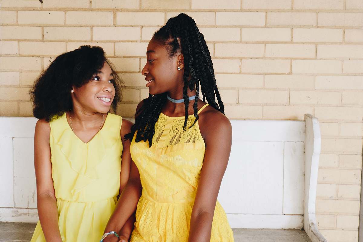 human two girl's in yellow sleeveless dresses sitting on white wooden bench during daytime person