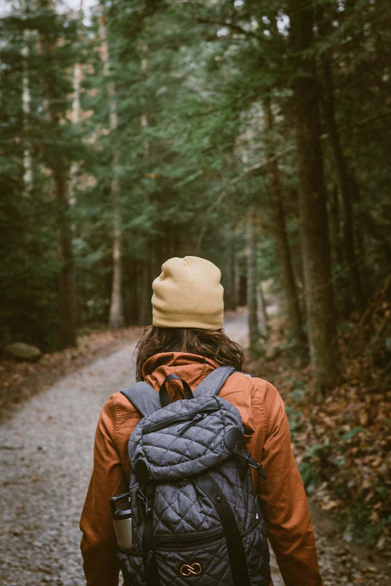 person woman carrying backpack walking towards the forest backpack