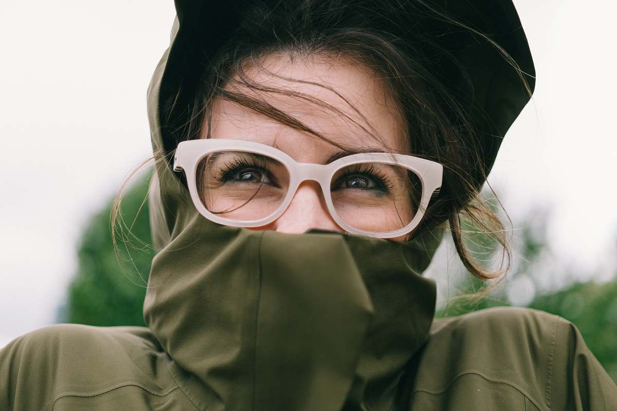 person woman covering mouth with green turtleneck top glasses