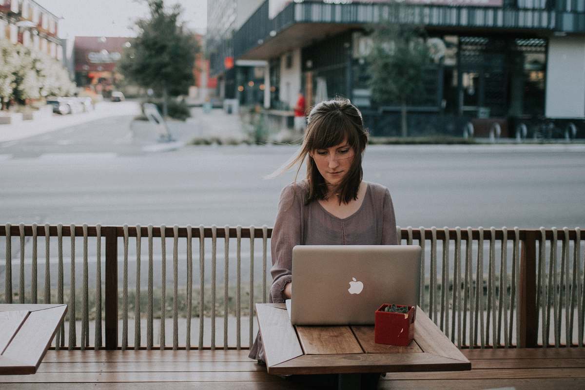 computer woman in gray shirt sitting on bench in front of MacBook laptop