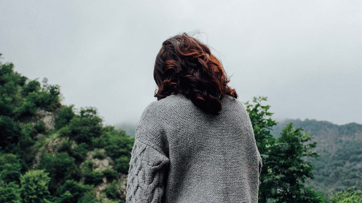 person woman in gray sweater standing in front of trees during daytime back