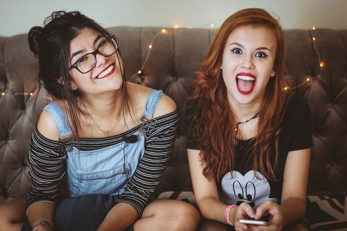 person woman laughing beside woman smiling sitting on tufted sofa inside the room human