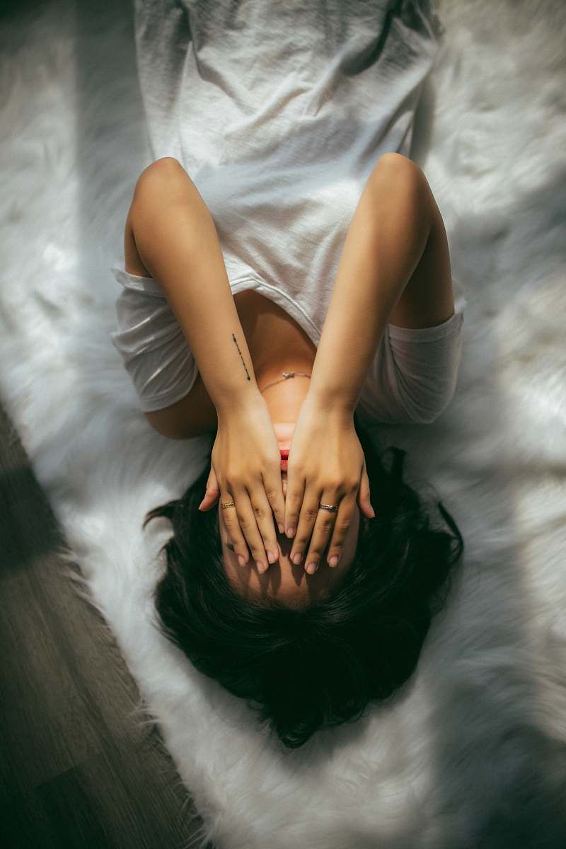 human woman laying down wearing white V-neck top covering eyes person