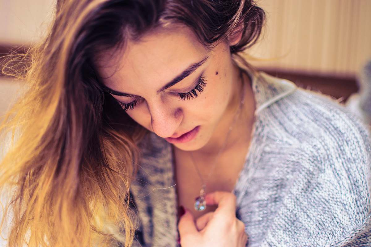 person woman looking down while holding necklace pendant human
