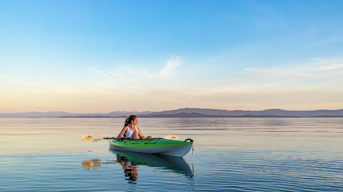 boat woman on green and white kayak holding yellow oar under white clouds and blue sky kayak