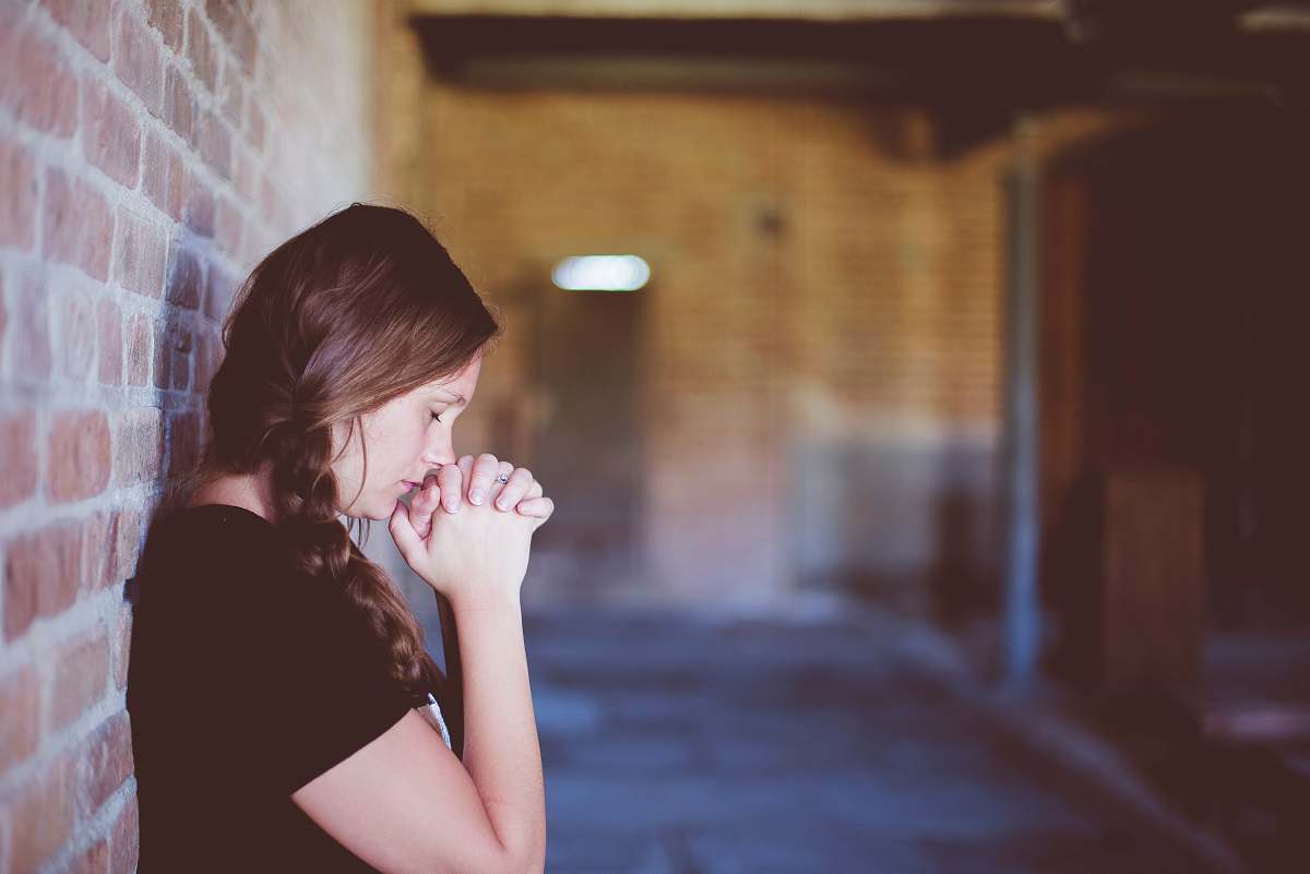 woman woman praying while leaning against brick wall girl