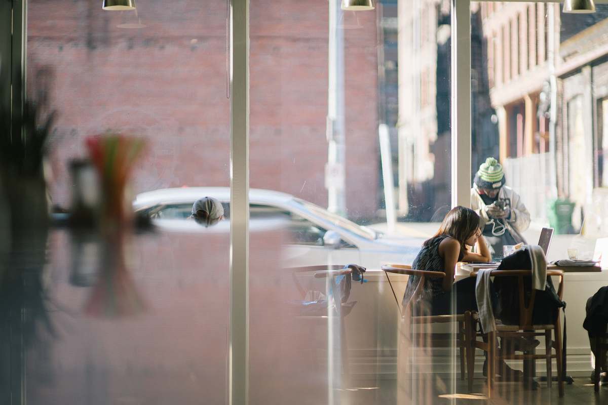 person woman sitting on chair near man holding device beside white post at daytime coffee shop